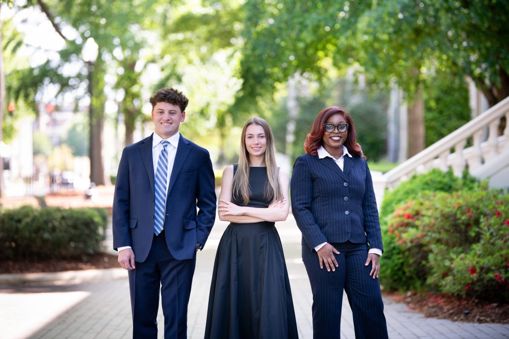 Three student smiling for the camera posed in an outdoor setting.